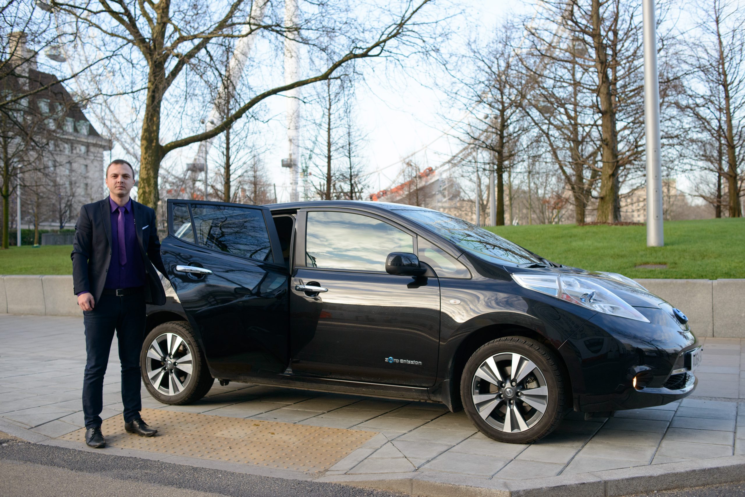 A photo of a an electric car with a driver standing outside.